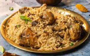 Close-up of aromatic chicken biryani served on a brass plate with garnishes, showcasing Indian culinary art.